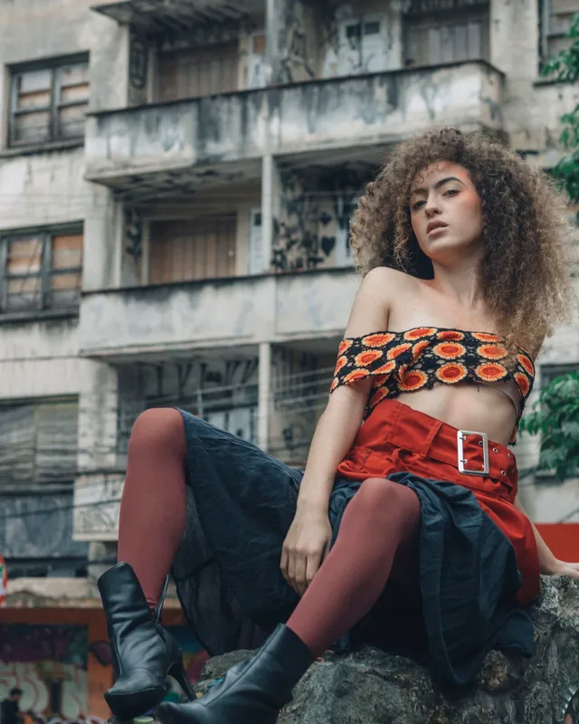 Modelo con top tejido al crochet naranja y negro, pollera roja con cinturón y botas negras — indumentaria de moda para mayoristas de ropa que venden al por mayor con su tienda B2B VentasxMayor