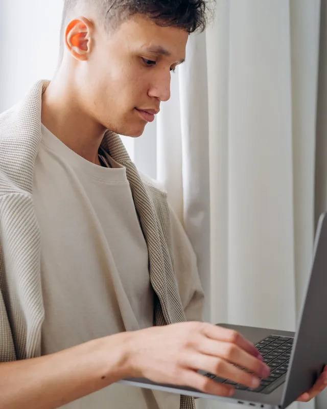 Hombre joven trabajando de pie con una laptop junto a la ventana — tecnología y electrónica para distribuidores que venden por mayor con su tienda mayorista B2B VentasxMayor